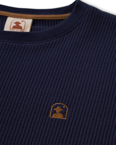 Close-up of The Cannes LS Waffle Knit Shirt - Luxe Navy by Dandy Del Mar, featuring a brown embroidered silhouette logo on the chest and a brown-trimmed collar in soft waffle knit fabric.