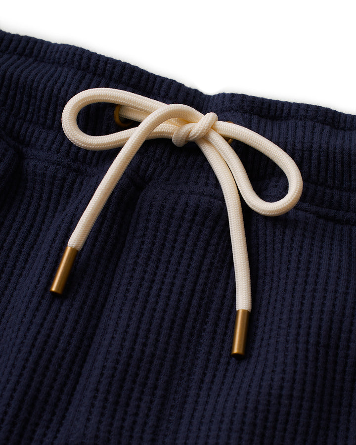 A close up of The Cannes Short - Luxe Navy sweatpants with a gold tie by Dandy Del Mar.