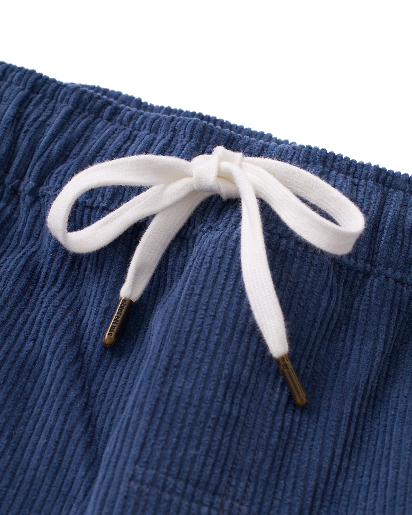 Close-up of a white drawstring looped into a bow on a pair of blue The Corsica Corduroy Pant - Moontide from Dandy Del Mar, featuring an elastic waist and made from 8-Wale corduroy.