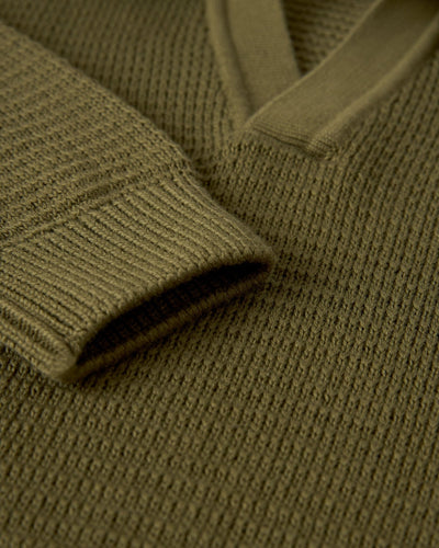 Close-up of The Sebastian LS Polo Shirt - Arbequina by Dandy Del Mar, an olive green cotton sweater-knit long sleeve polo, highlighting the sleeve and v-neck collar detail from our knitwear collection.