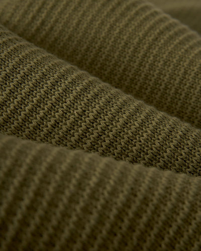 Close-up of the Sebastian LS Polo Shirt - Arbequina by Dandy Del Mar, featuring ribbed, olive green sweater-knit cotton fabric with a textured pattern and horizontal ridges.