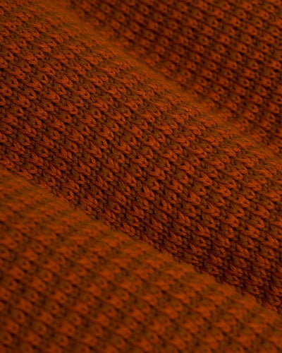 Close-up of The Sebastian LS Polo Shirt in Burnt Sienna by Dandy Del Mar, showcasing its textured knit fabric with a repeating ribbed pattern—an ideal men's knitwear piece.