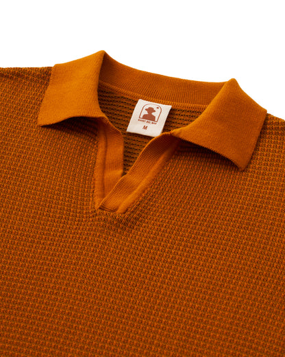 The Sebastian Long Sleeve Polo in Burnt Sienna by Dandy Del Mar features a V-neck, collar, and long sleeves. Crafted from 100% cotton for comfort, it includes a small inner label with the logo and size "M.