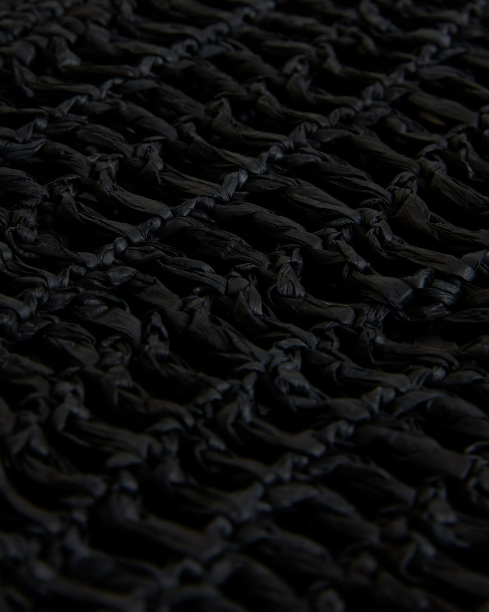 Close-up of a textured black Dandy Del Mar raffia-effect yarn fabric with intricate knot detailing, featuring The Amabile Raffia Bag in Onyx.