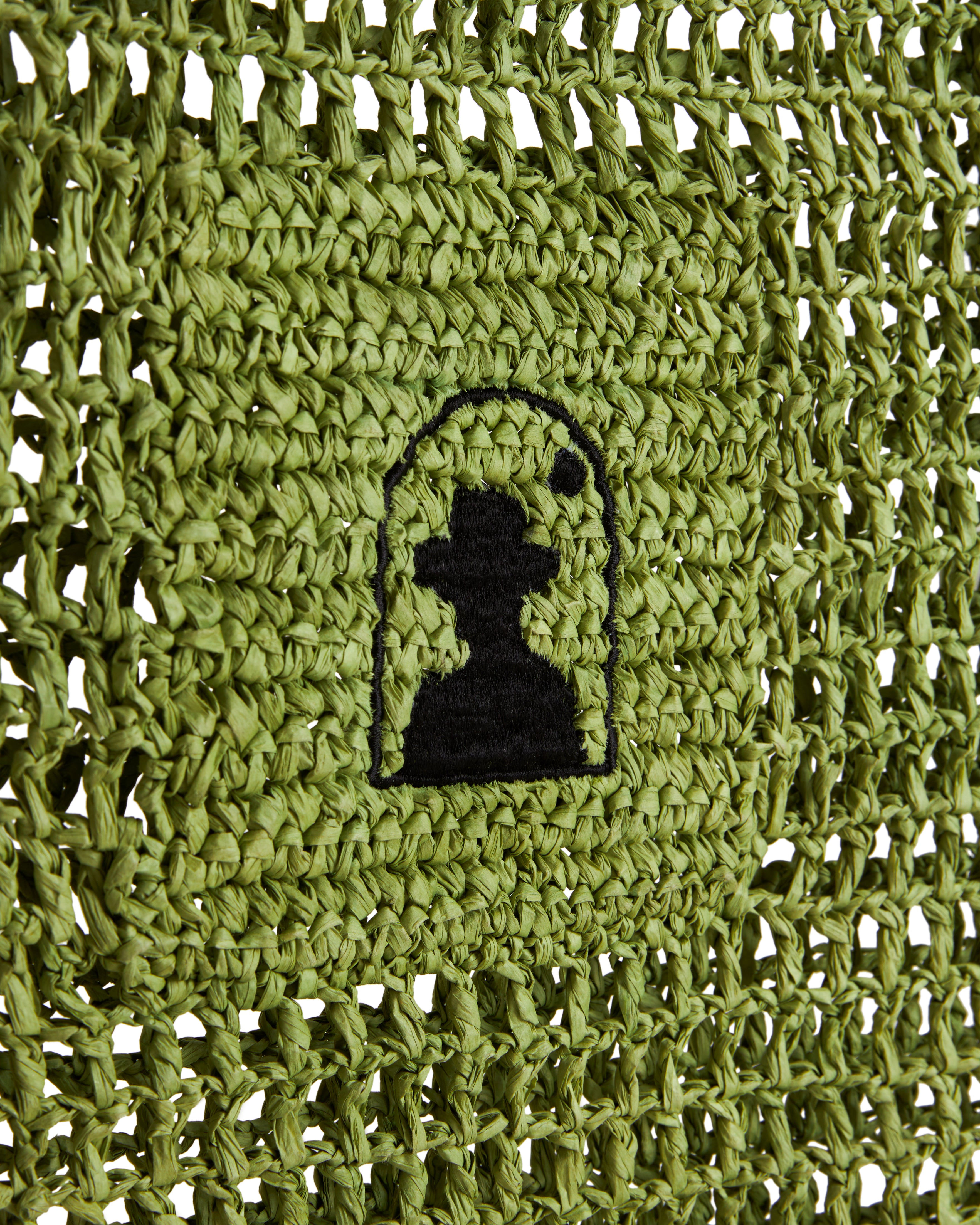 Green crochet design featuring a black silhouette of a person wearing a hat, enclosed in an arch, crafted with raffia-effect yarn, inspired by The Amabile Raffia Bag - Verde from Dandy Del Mar.