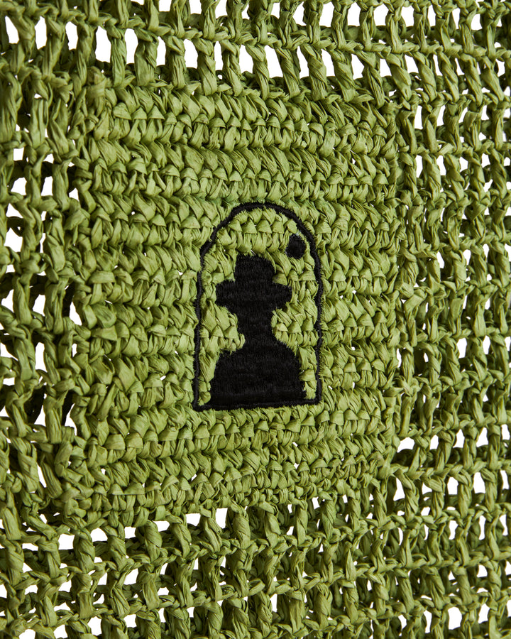 Close-up of a green knitted fabric featuring a black embroidered logo of The Amabile Raffia Bag by Dandy Del Mar.