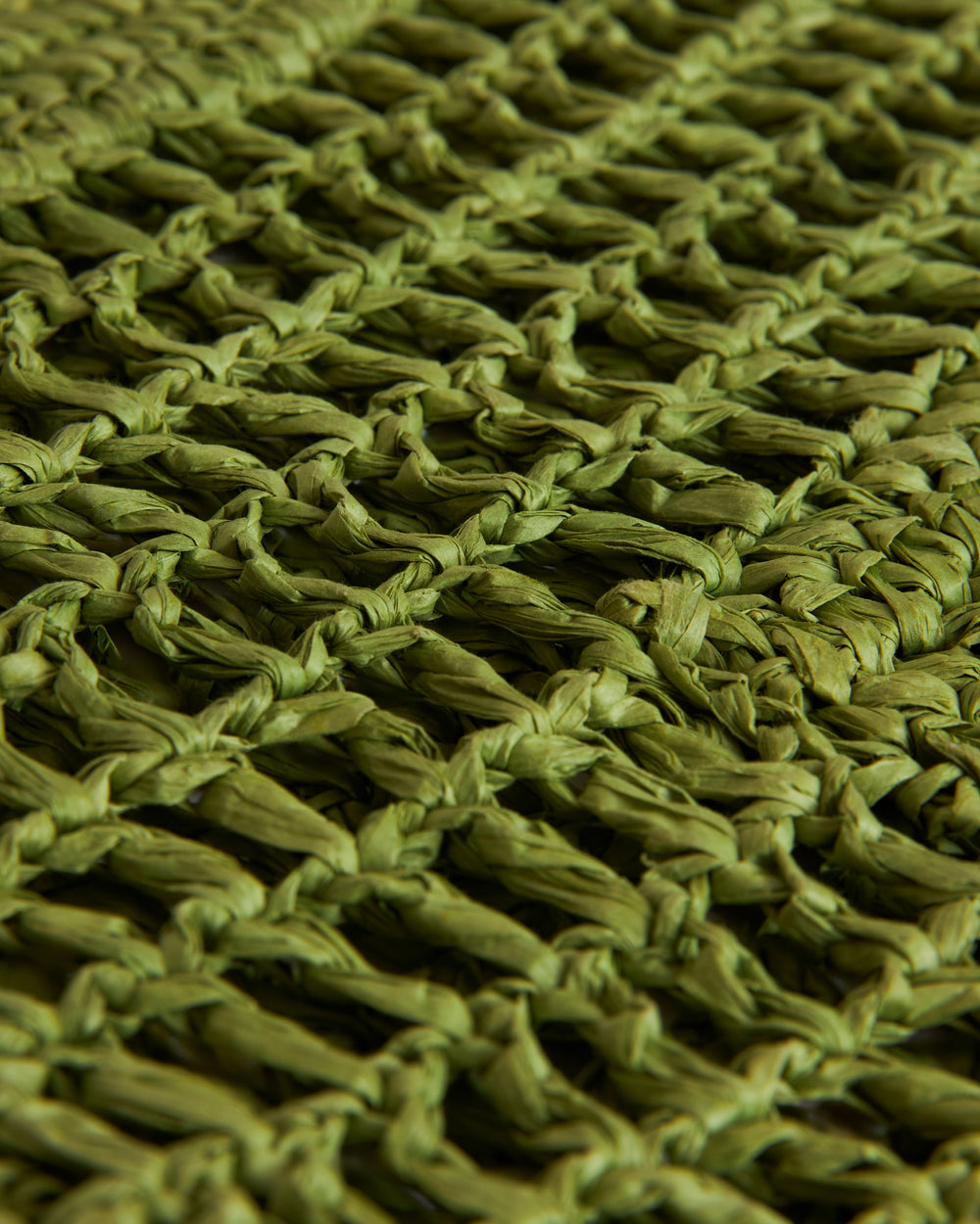 Close-up view of a textured green woven fabric showing intricate details of the weave pattern, featuring The Amabile Rafia Bag from Dandy Del Mar.