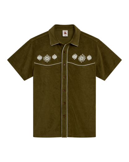 The Gaucho Shirt - Arbequina by Dandy Del Mar features short sleeves, olive green fabric, white floral chest embroidery, and white piping on seams and pockets—ideal for an Equatorial Cowboy style.