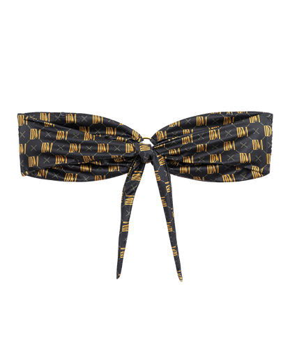 The Gomera Top - Oro Monogram by Dandy Del Mar is a black strapless bandeau bikini top featuring a front tie and gold geometric IDM logo pattern, crafted from recycled polyamide.
