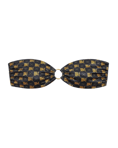 The Gomera Top - Oro Monogram by Dandy Del Mar features gold "IDM" logos and a central metal ring on black Carvico VITA fabric, shown against a plain black background.
