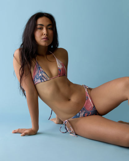 Woman wearing The Kokomo Bottom - Lantana by Dandy Del Mar sits on the floor against a light blue background, leaning on one arm with her legs extended and crossed.