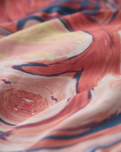A close-up of The Elba One Piece - Lantana by Dandy Del Mar, showing its red, yellow, and navy blue abstract swirl pattern and soft folds—a sophisticated swimwear choice.