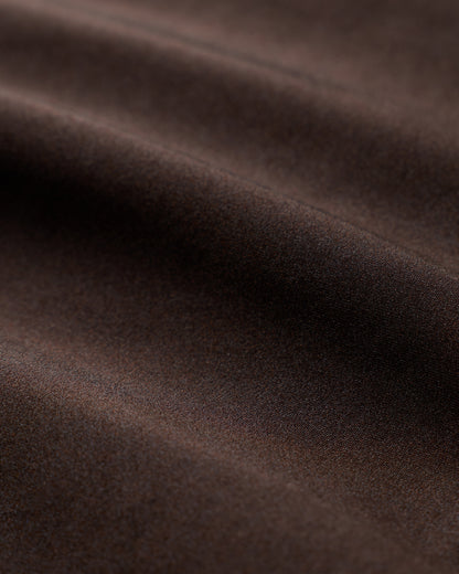 Close-up of the smooth brown fabric from The Elba One Piece - Tierra by Dandy Del Mar, featuring gentle folds that echo the elegant strapless silhouette and moderate coverage of this luxurious swimsuit. Soft shadows highlight its rich texture.
