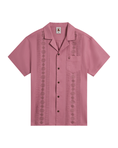 The Brisa Linen Shirt - Dawn by Dandy Del Mar features short sleeves, a button-up front, pink linen with gardenia floral embroidery, coconut shell buttons, and a chest pocket, displayed on a plain black background.