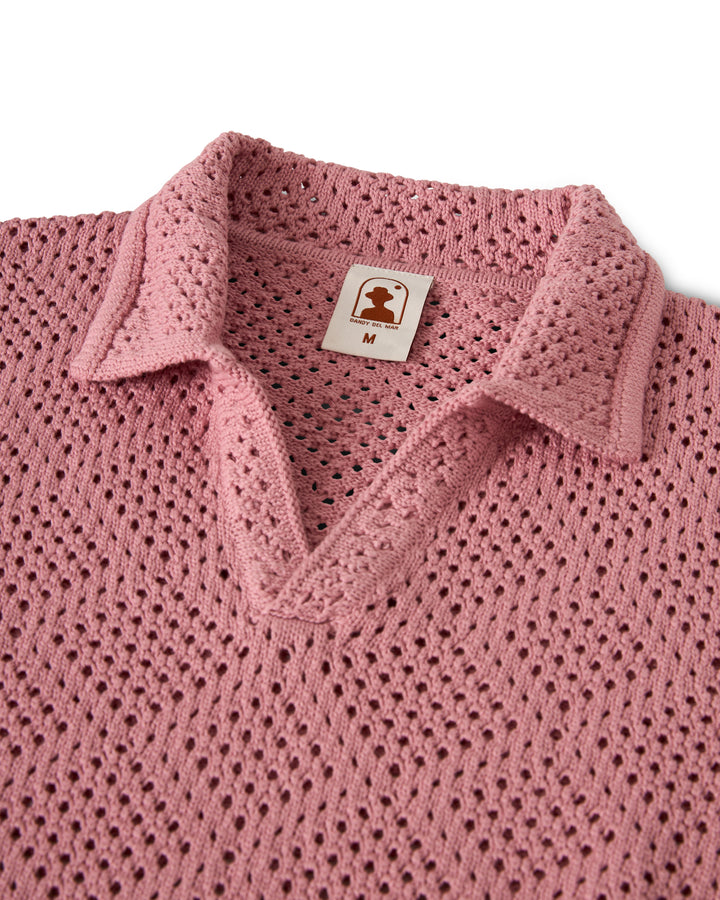 A pink crochet shirt with collar and V-neck, featuring a brown Dandy Del Mar brand tag with "M" inside, called The Antibes Crochet Shirt - Dawn.