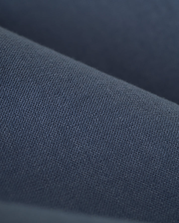 Close-up of a textured dark blue fabric, showcasing the detailed weave pattern of The Brisa Linen Pant - Moontide by Dandy Del Mar, ideal for a relaxing vacation.