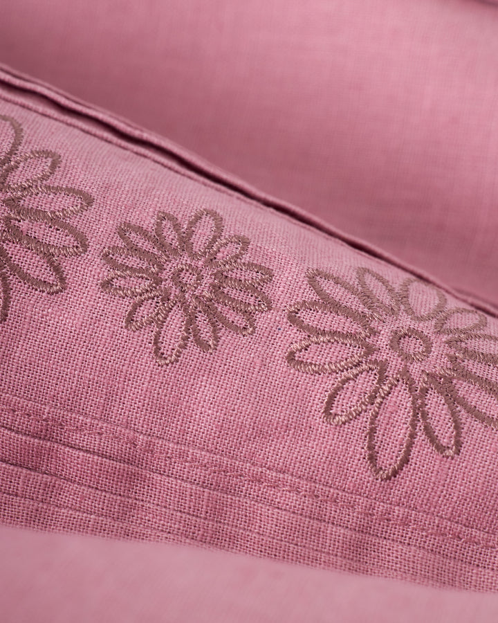 Close-up of The Brisa Linen Shirt - Dawn by Dandy Del Mar, featuring pink fabric with embroidered floral patterns and stitching details.