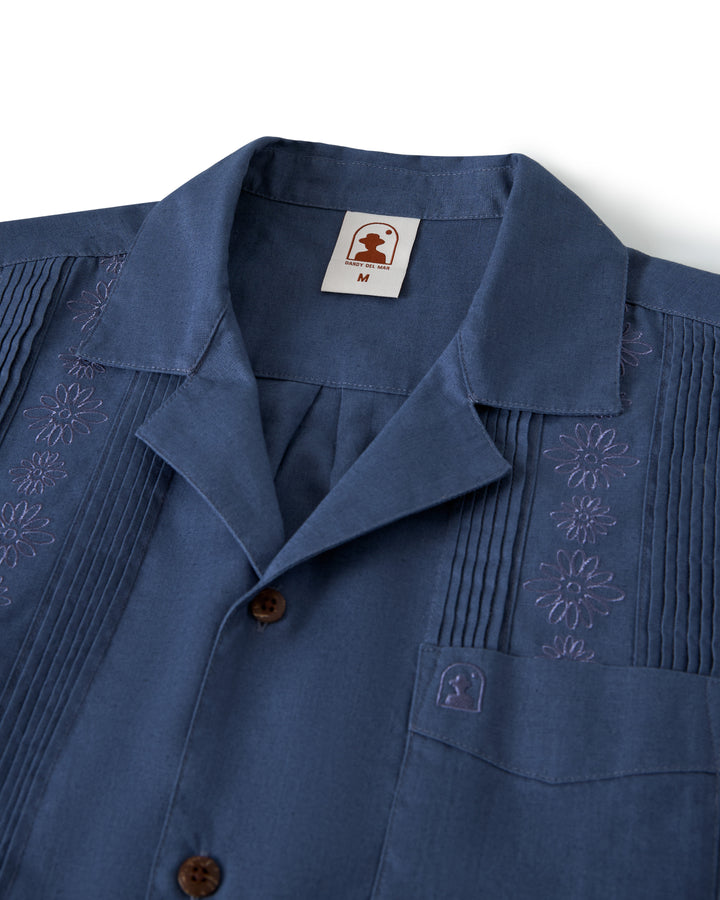 The Brisa Linen Shirt - Moontide by Dandy Del Mar features decorative embroidery, a small chest pocket, and brown buttons with a size "M" label inside the collar.