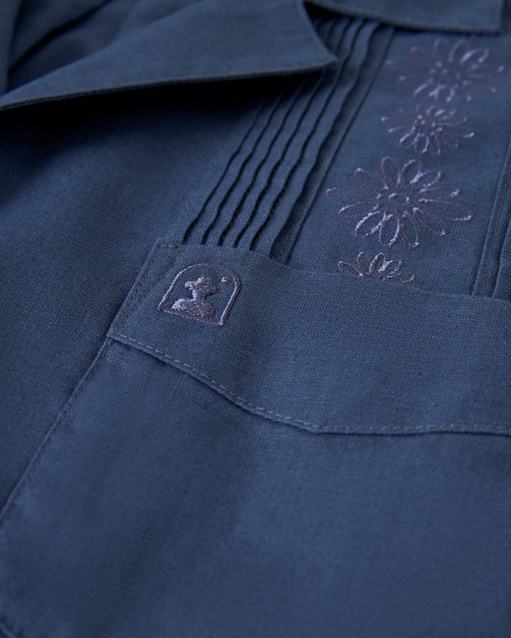 Close-up of The Brisa Linen Shirt - Moontide by Dandy Del Mar, showcasing floral embroidery and pintuck detailing in dark blue.