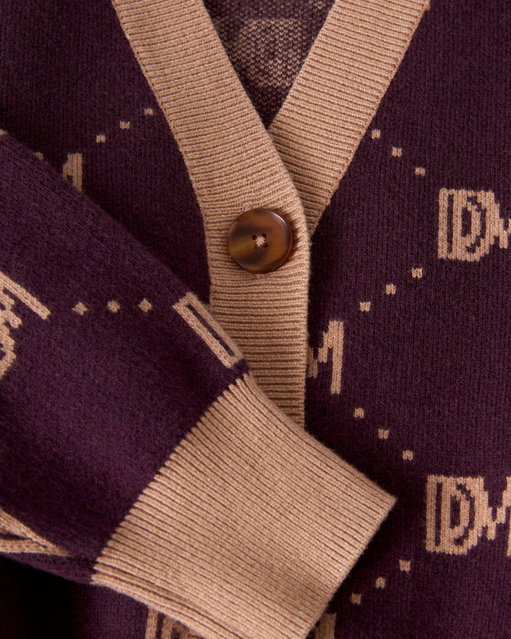 Close-up of The Canela Cardigan - Amethyst from Dandy Del Mar, showcasing a maroon cotton design with beige trim and button, adorned with a stylish monogram pattern.