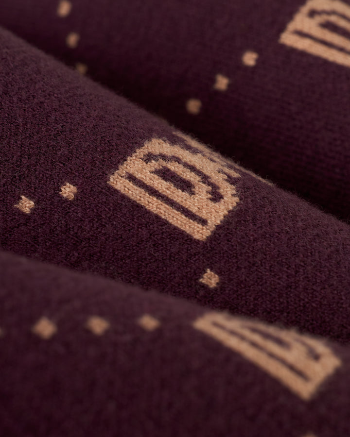 Close-up of The Canela Cardigan - Amethyst by Dandy Del Mar, a dark cotton cardigan featuring a pattern of light brown geometric shapes and dots, showcasing a unique monogram design.