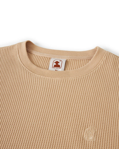 The Cannes LS Waffle Knit Shirt in Truffle by Dandy Del Mar features a beige waffle-knit fabric, crewneck design, small embroidered logo near the hem, and an inner collar tag.