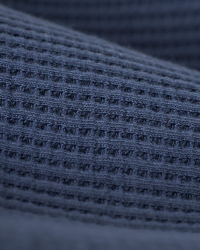 Close-up of The Cannes Waffle Knit Polo Shirt - Moontide by Dandy Del Mar, showcasing its textured blue waffle knit fabric with a distinct grid-like pattern.
