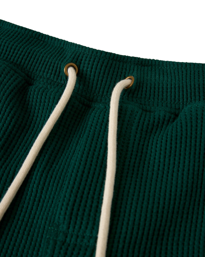 Close-up of The Cannes Waffle Knit Shorts - Albero by Dandy Del Mar, featuring green corduroy fabric with two white drawstrings through brass grommets.