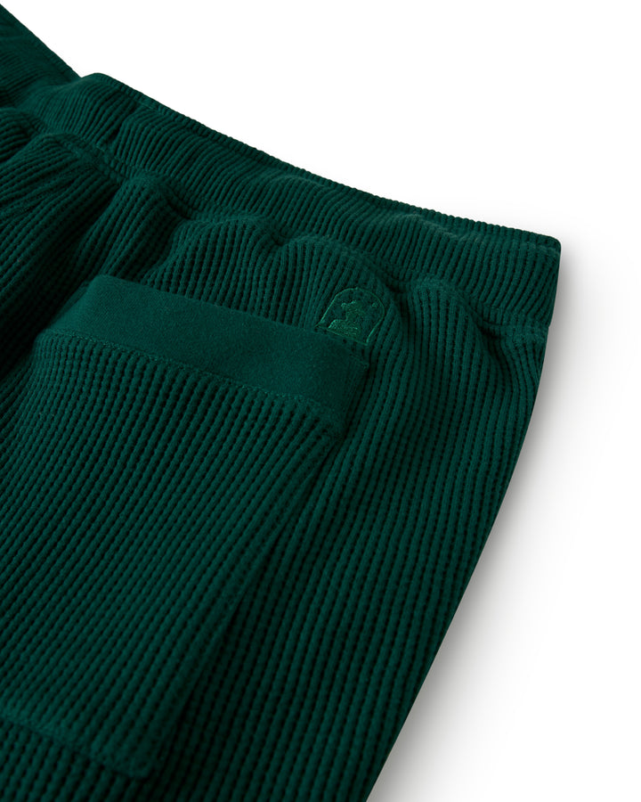 Close-up of The Cannes Waffle Knit Shorts - Albero by Dandy Del Mar, featuring green ribbed fabric with a pocket and embossed detail above it.