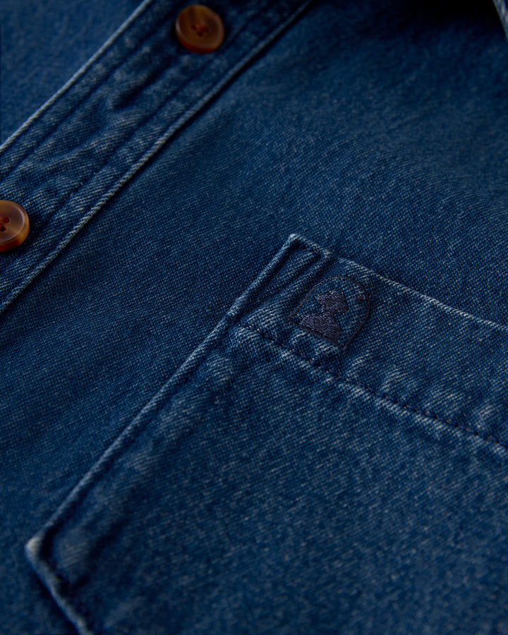 Close-up of The Cartagena Denim Shirt - Indigo by Dandy Del Mar pocket with visible stitching detail, tailored fit, and brown buttons.