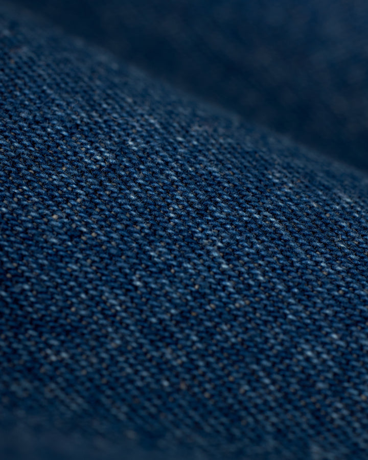 Close-up image of indigo denim fabric from The Cartagena Denim Shirt by Dandy Del Mar, displaying detailed texture with visible weave patterns and tailored fit features.