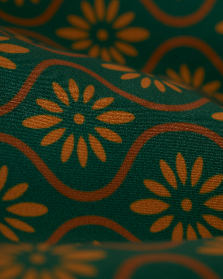 Close-up of The Cassis Square-Cut Swim Brief - Albero by Dandy Del Mar, showcasing a green background with orange floral patterns and wavy lines.