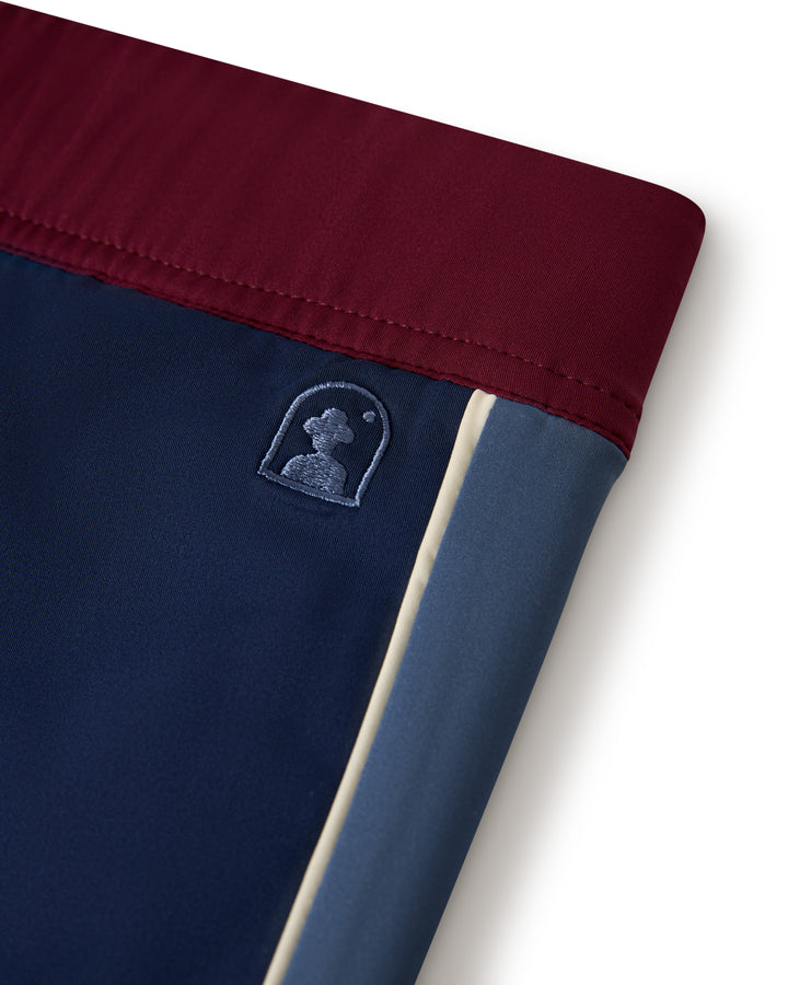 Close-up of The Cassis Square-Cut Swim Brief - Anchor by Dandy Del Mar, showcasing a maroon waistband and navy blue fabric. Features a small embroidered logo of a person's silhouette on the side.