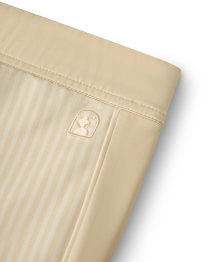 Close-up of a beige striped fabric featuring a stitched emblem with a profile on a rounded rectangle, reminiscent of the luxurious style in Dandy Del Mar's The Cassis Square Cut Swim Brief - Sabbia.