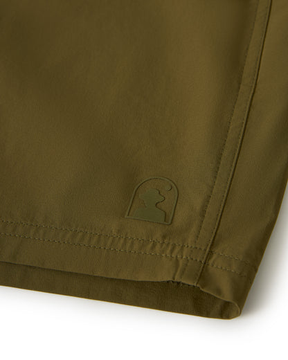 Close-up of The Cavoli Swim Short - Berdea in olive green by Dandy Del Mar, featuring a small embroidered logo of a stylized figure near the edge, designed for comfort and durability in any setting.