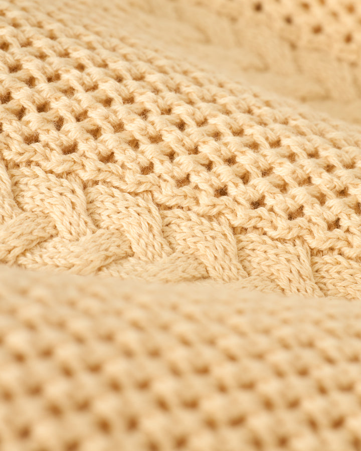 A close-up of The Crete Crochet Cardigan - Sabbia by Dandy Del Mar showcases its beige textured pattern of interwoven stitches.