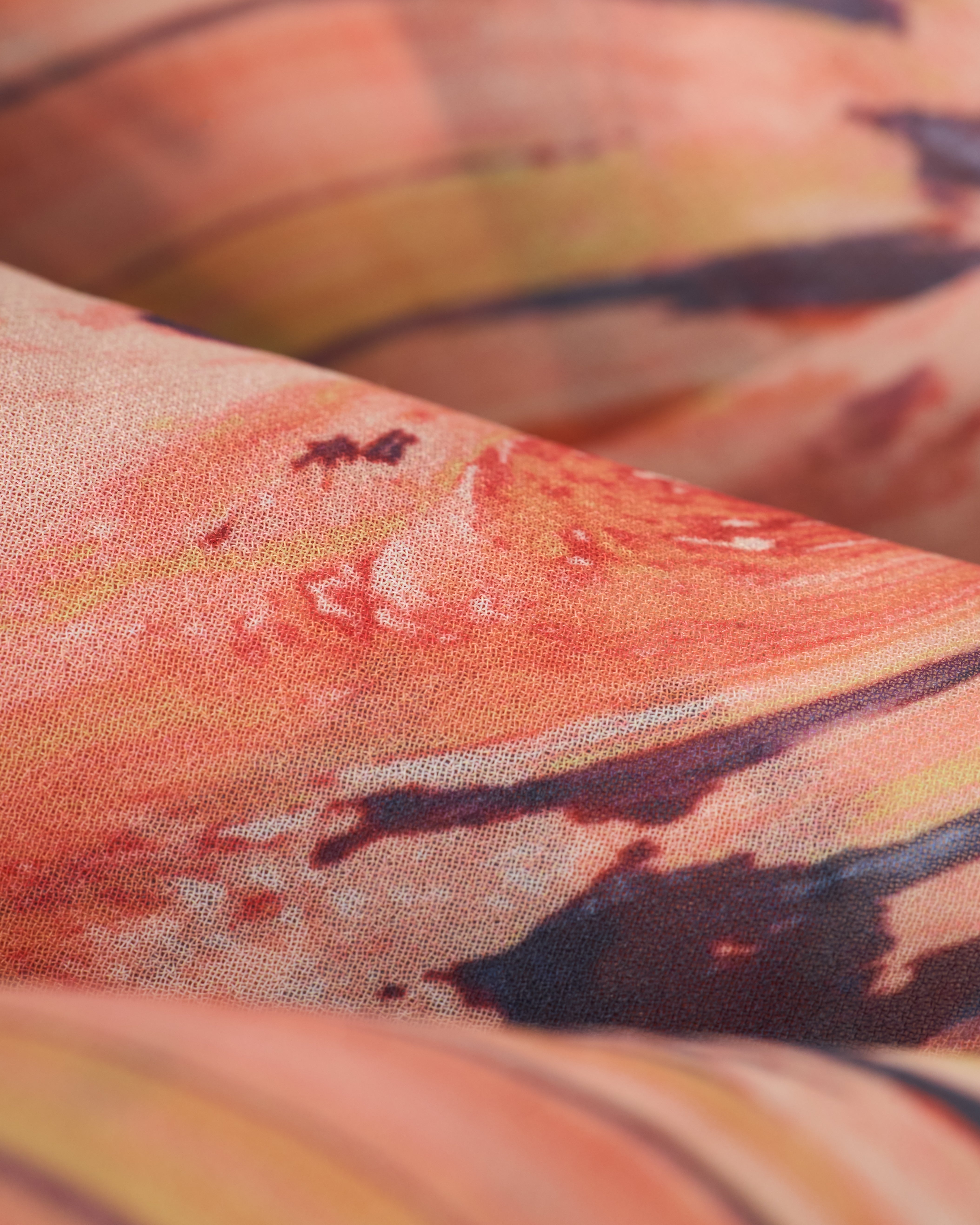 Close-up of The Curacao Short - Lantana by Dandy Del Mar, showcasing an abstract swirl pattern in orange, pink, and black.