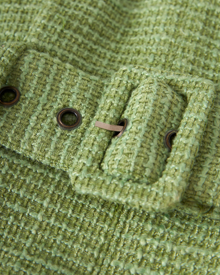 Close-up of the textured green fabric on The Trinidad Tweed Strapless Dress in Oliva by Dandy Del Mar, showcasing a rectangular buckle and metal eyelets on the waist belt.