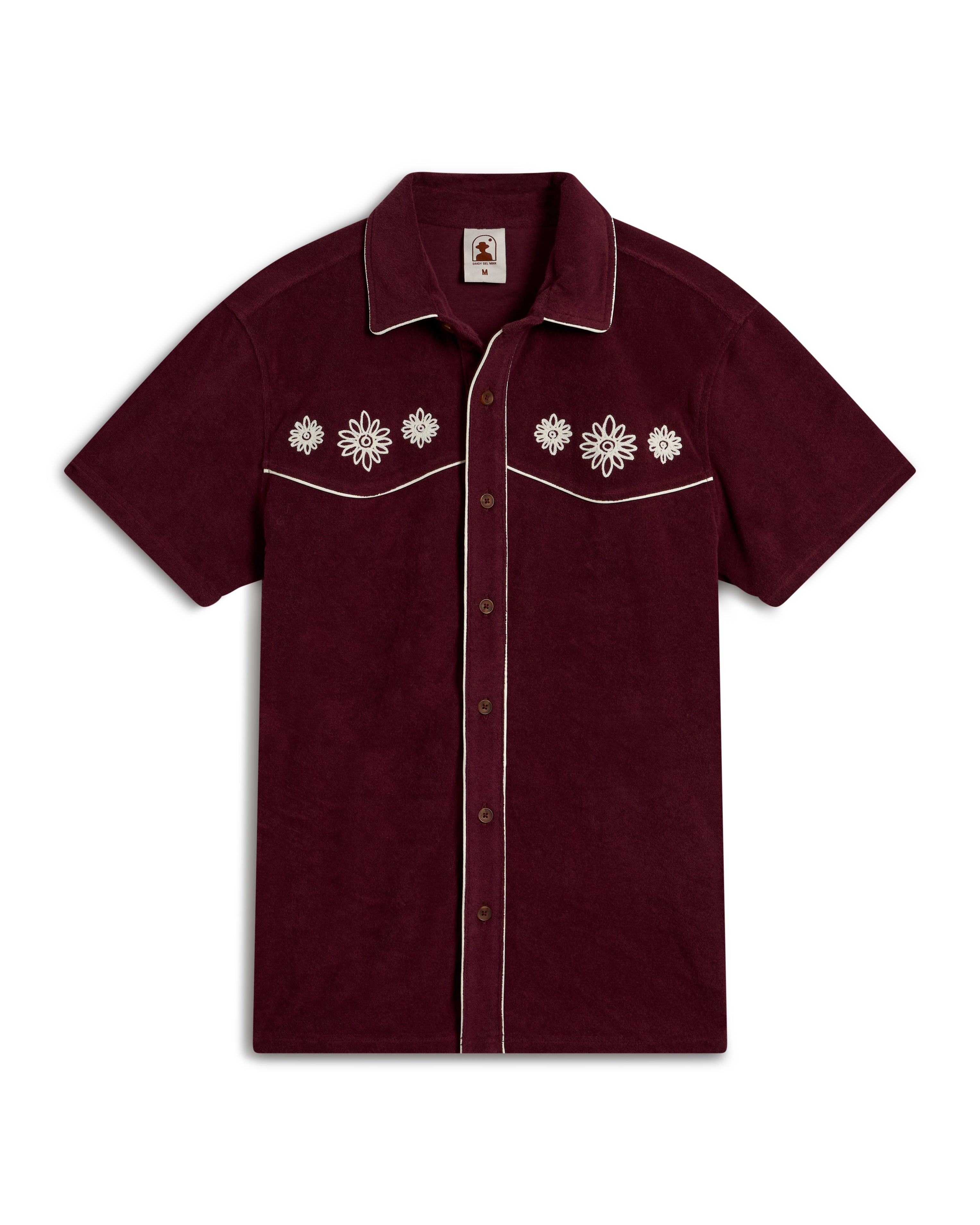 Channel an Equatorial Cowboy style with Dandy Del Mar's The Gaucho Shirt - Bordeaux, a maroon short-sleeve shirt with white floral embroidery on the chest, white piping on the edges and pockets, and brown buttons down the front for a bold twist on classic fashion.