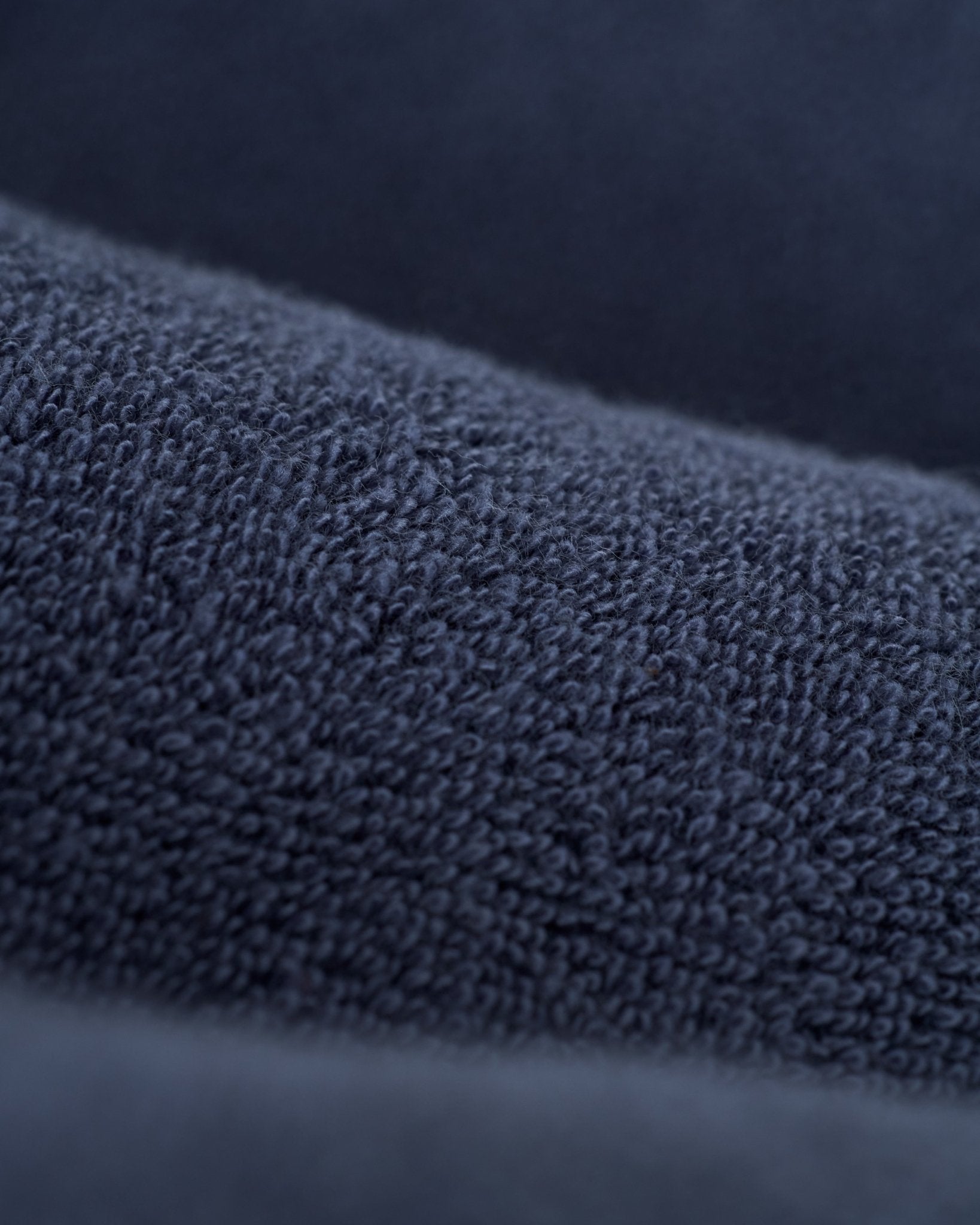 A close-up of The Gaucho Shirt - Moontide by Dandy Del Mar shows its dark blue, textured terry cloth with a soft, looped surface, echoing the Equatorial Cowboy style.