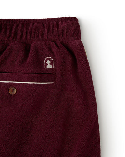 A close-up of The Gaucho Short - Bordeaux by Dandy Del Mar shows burgundy fleece pants with an elastic waistband, a single back pocket with button closure, and a small logo above it, capturing the relaxed style.