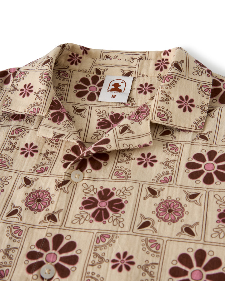 The Grenadine Crinkle Gauze Shirt - Sabbia by Dandy Del Mar is a beige shirt with a floral and geometric pattern in brown and pink, featuring a collared neckline and front buttons.