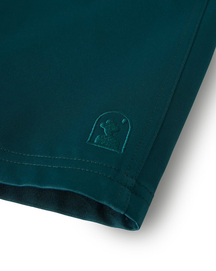 Close-up of a teal fabric from Dandy Del Mar's The Mallorca Swim-Walk Short in Tempest Blue, featuring an embroidered abstract logo. Made with nylon construction, it includes adjustable brass side fasteners for a perfect fit.