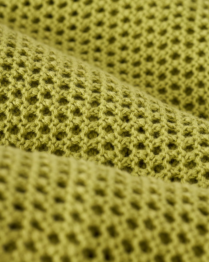 Close-up of The Malta Crochet Dress - Verde by Dandy Del Mar, showcasing its textured green fabric with a waffle weave pattern.