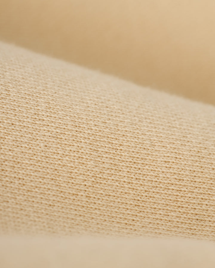 Close-up of a beige knitted fabric with visible texture and stitches, evoking The Marseille French Terry Pullover in Sabbia by Dandy Del Mar.