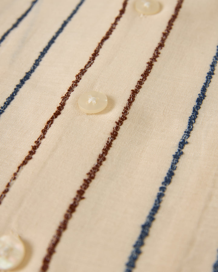 Close-up of The Quarta Shirt - Scallop Weave by Dandy Del Mar, featuring blue and brown vertical stripes with small white buttons.