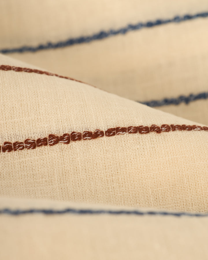 Close-up of The Quarta Shirt - Scallop Weave by Dandy Del Mar, featuring beige fabric with horizontal brown and blue embroidered lines.