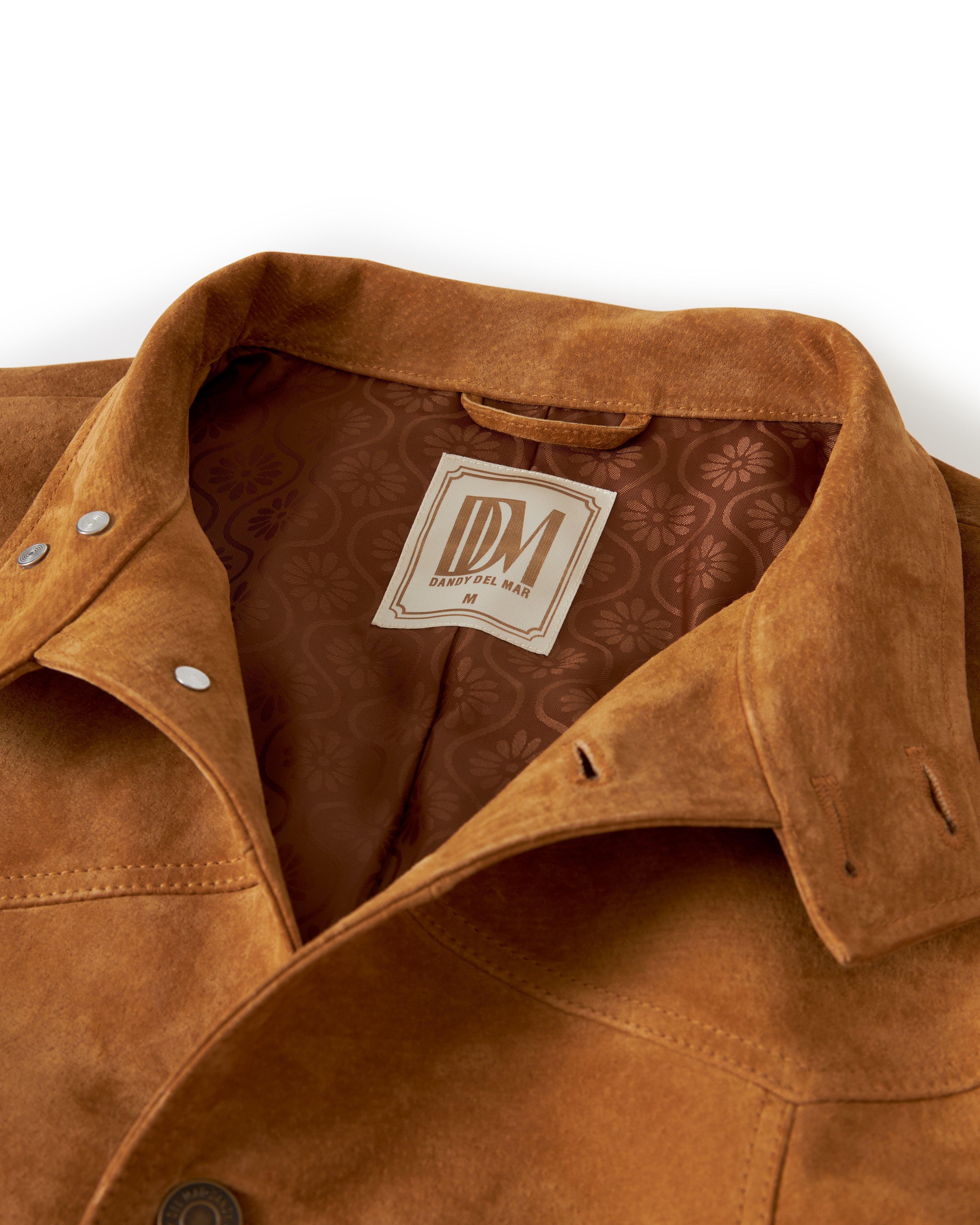 Close-up of The San Juan Suede Leather Jacket - Sable, crafted from luxurious suede leather by Dandy Del Mar, featuring a jacquard lining and a label with "DM." The collar and some of the front buttons are visible.