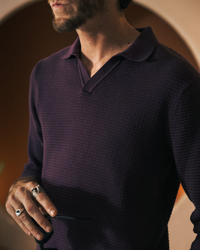 A man wearing the Dandy Del Mar The Sebastian LS Polo Shirt in Amethyst holds scissors in one hand, rings visible on his fingers.