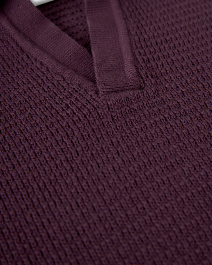 Close-up of the Sebastian Long Sleeve from Dandy Del Mar, featuring a deep purple, textured knit fabric with amethyst tones and a V-neck design. The Sweater-Knit Cotton fabric has a ribbed pattern and a smooth, slightly raised trim along the neckline.